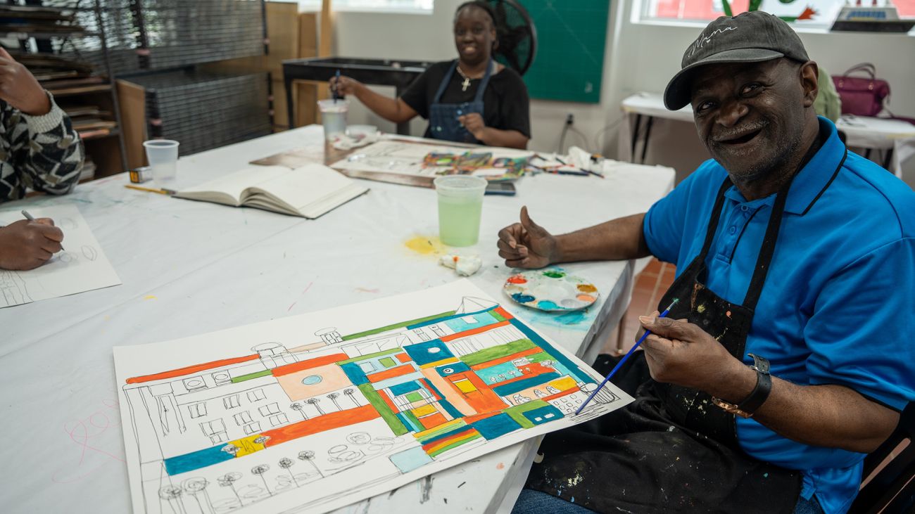 Artist Ray Smith works on a piece at PASC’s Detroit studio. Jotina Ballard is in the background drawing at a white table.